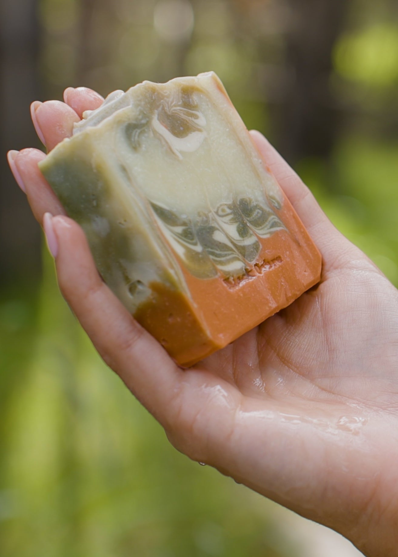 Hand holding a bar of soap with a natural, blurred green background