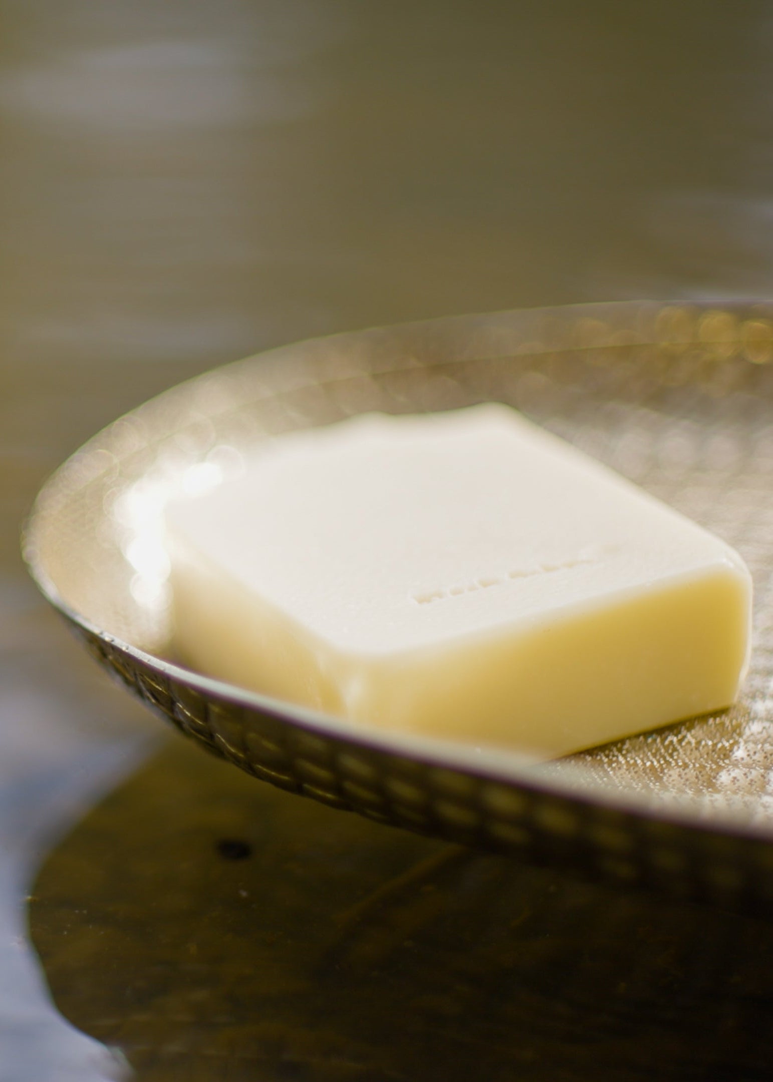 Bar of soap on a textured metal tray with water in the background