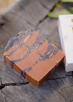 Bar of soap with a decorative pattern on a wooden surface next to its packaging.